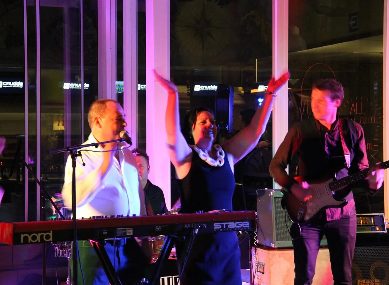 Een band speelt in het sportcentrum; de zangeres steekt haar armen in de lucht