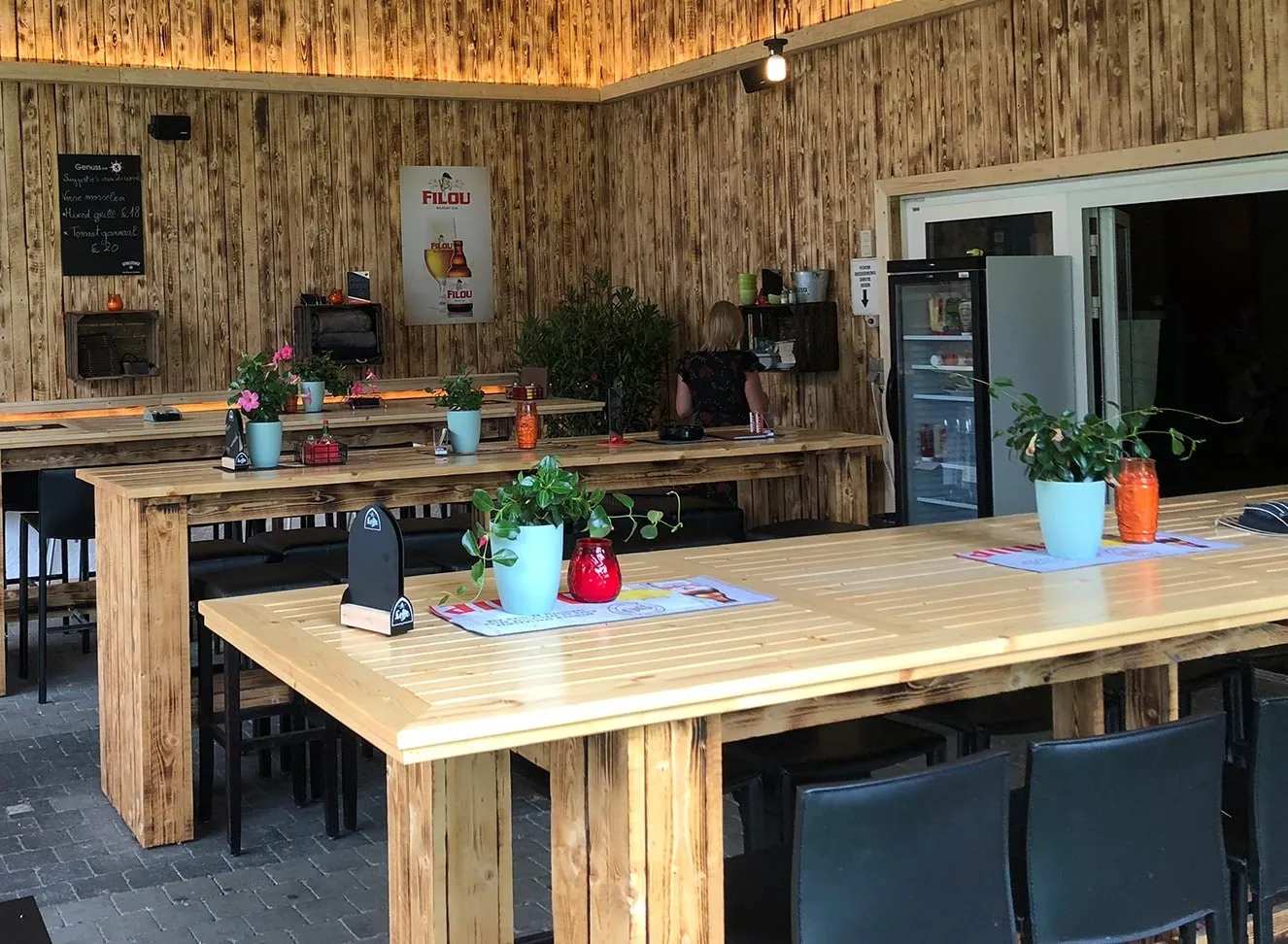 Het overdekte terras met houten wanden en lange tafels, overdag