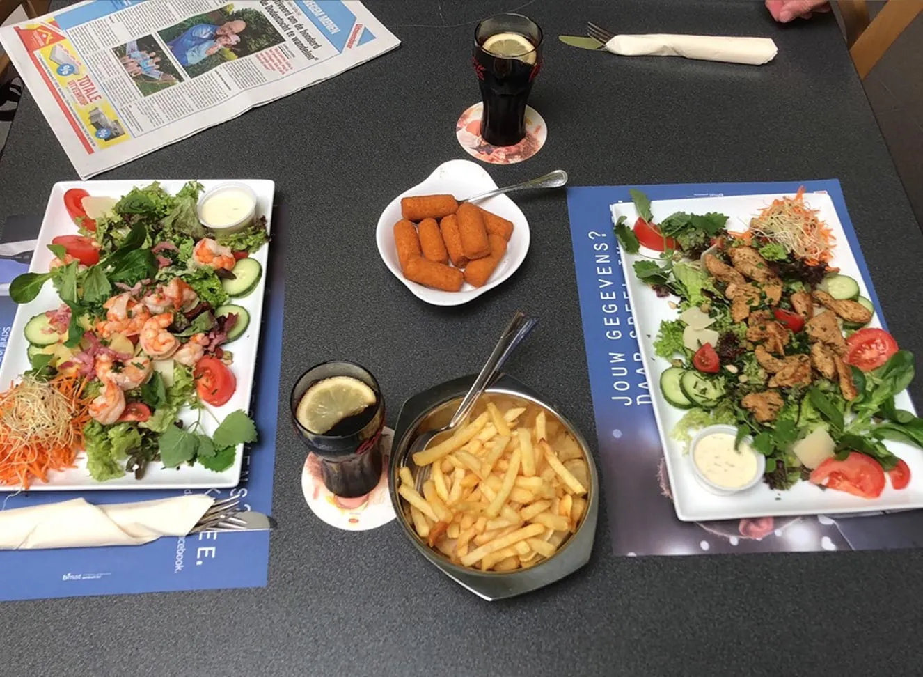 Slaatjes met scampi en kip, kroketjes en een kom frietjes op tafel