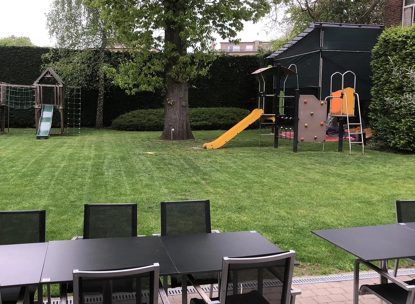 De speeltuin met glijbaan op het gras, achter de terrastafels